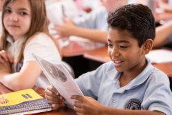 A learner smiling as he reads school curriculum