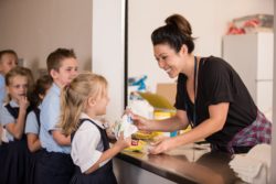 A faculty member handing snacks to elementary school children